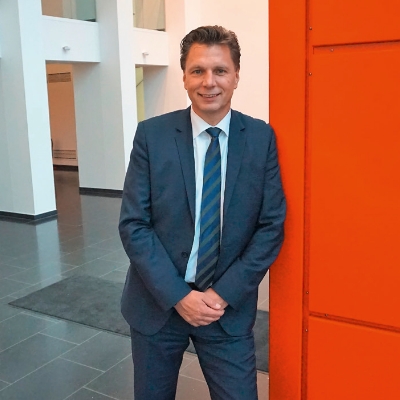 Thorsten Kinhöfer, Managing Director Container Terminal Herne Thorsten Kinhöfer in a blue suit leans against an orange wall.
